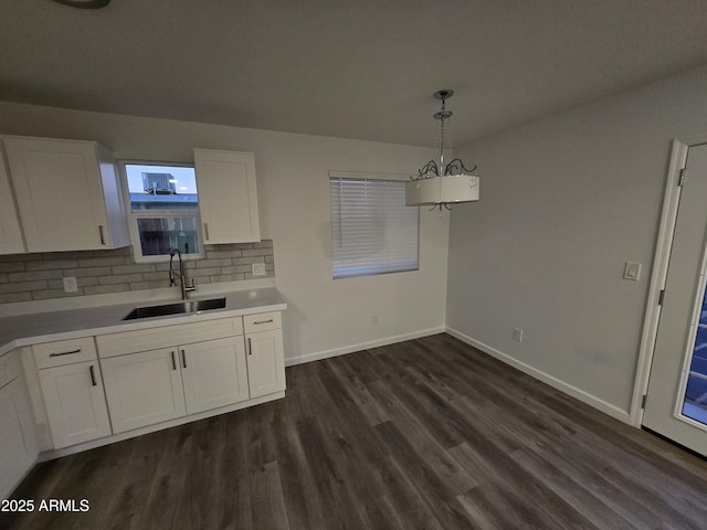 kitchen featuring sink, white cabinets, backsplash, hanging light fixtures, and dark wood-type flooring