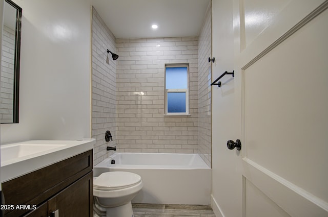 full bathroom with hardwood / wood-style flooring, tiled shower / bath, vanity, and toilet