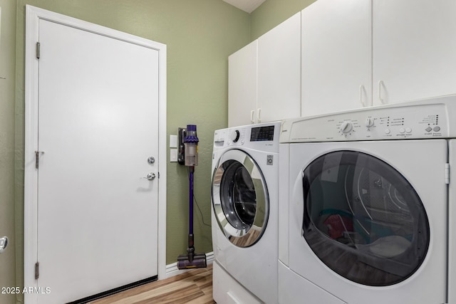 clothes washing area featuring separate washer and dryer, light hardwood / wood-style floors, and cabinets