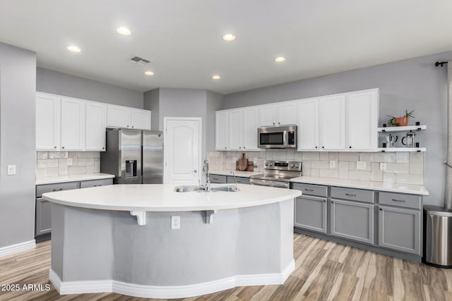 kitchen with an island with sink, stainless steel appliances, gray cabinetry, backsplash, and sink