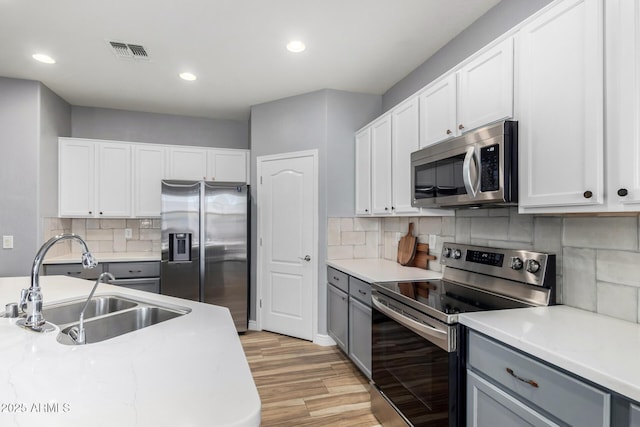 kitchen featuring stainless steel appliances, gray cabinetry, white cabinetry, and sink