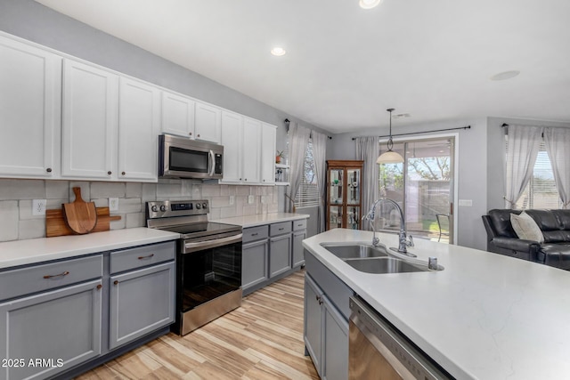 kitchen featuring gray cabinets, stainless steel appliances, decorative backsplash, hanging light fixtures, and sink