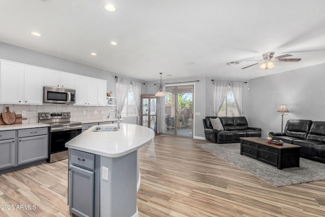 kitchen with pendant lighting, white cabinets, stainless steel appliances, an island with sink, and sink