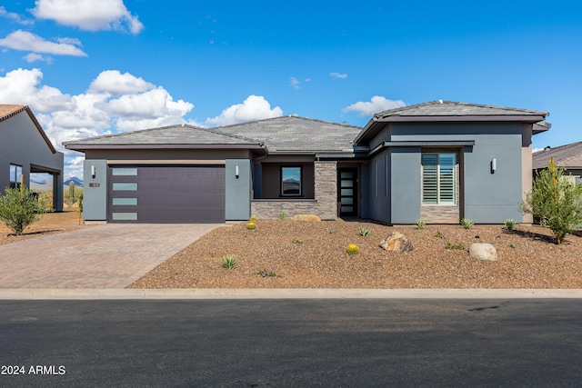 prairie-style home with a garage, stone siding, decorative driveway, and stucco siding