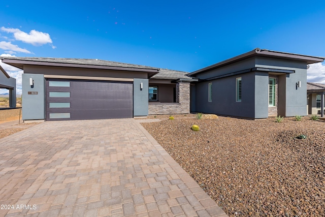 prairie-style house with stone siding, decorative driveway, an attached garage, and stucco siding