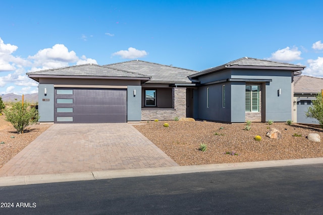 prairie-style home featuring a garage, stone siding, decorative driveway, and stucco siding