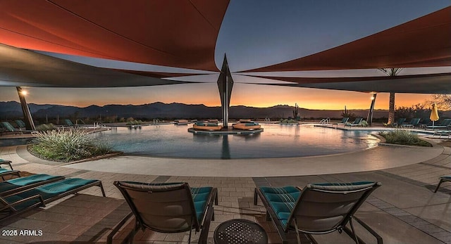 pool at dusk featuring a patio area, a community pool, and a water and mountain view