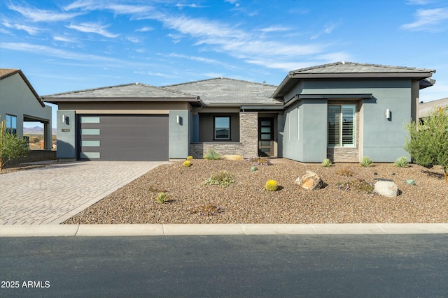 prairie-style home featuring a garage, stone siding, decorative driveway, and stucco siding