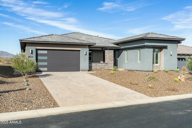 prairie-style home with stone siding, decorative driveway, an attached garage, and stucco siding