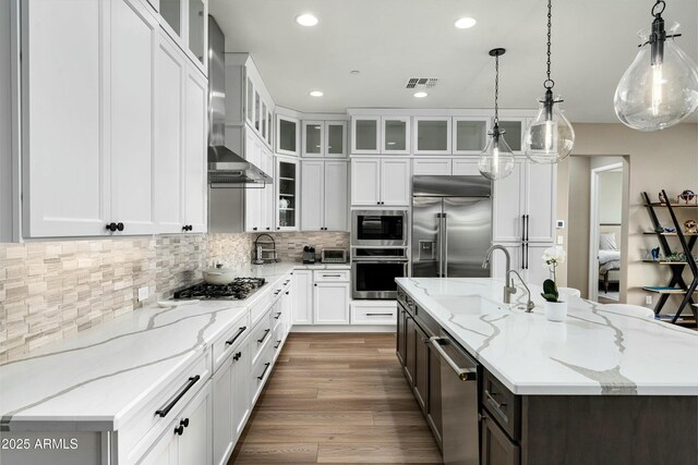 kitchen featuring a kitchen island with sink, white cabinets, decorative light fixtures, and built in appliances