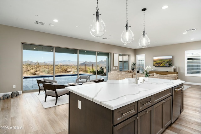 kitchen with visible vents, decorative light fixtures, light stone countertops, light wood-type flooring, and a sink