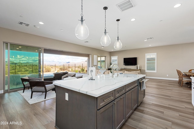 kitchen with a sink, visible vents, open floor plan, hanging light fixtures, and light stone countertops