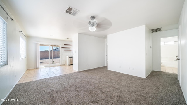 empty room featuring a ceiling fan, carpet flooring, visible vents, and tile patterned floors