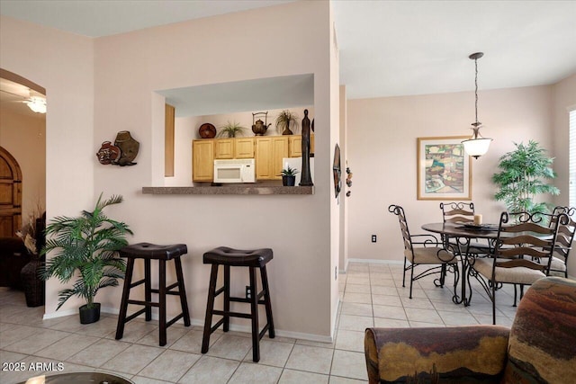 kitchen with pendant lighting, white appliances, light brown cabinets, a breakfast bar area, and light tile patterned floors