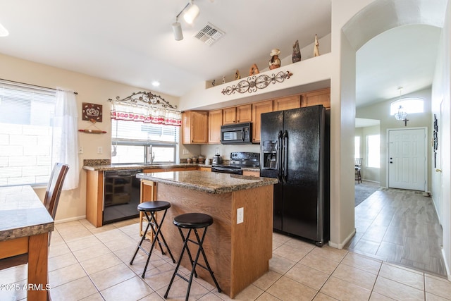 kitchen featuring visible vents, black appliances, a center island, and vaulted ceiling