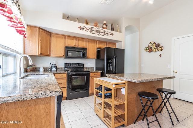 kitchen with a kitchen bar, black appliances, light tile patterned floors, and a sink