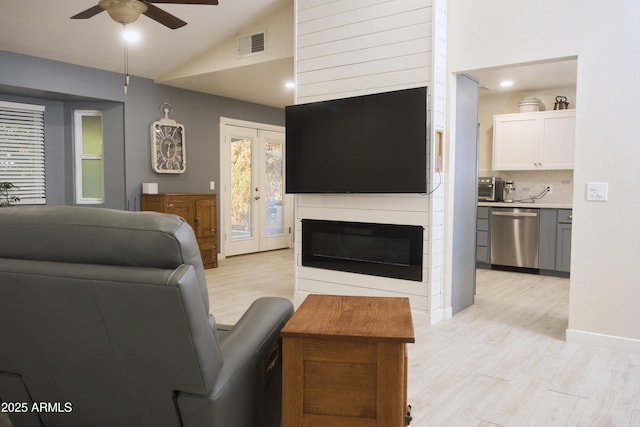 living room featuring light wood-style floors, visible vents, a ceiling fan, and vaulted ceiling