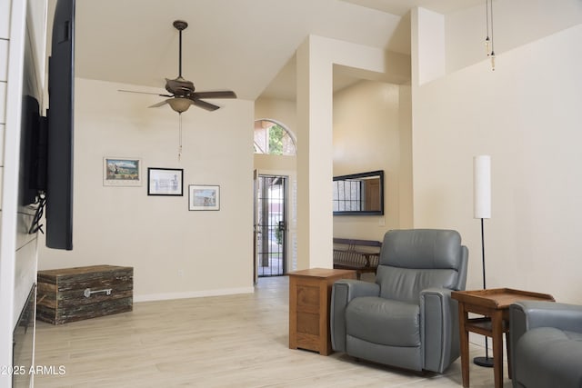 living area with light wood-type flooring, a high ceiling, baseboards, and ceiling fan