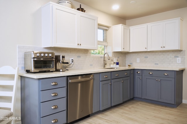 kitchen featuring light countertops, white cabinets, decorative backsplash, stainless steel dishwasher, and a sink