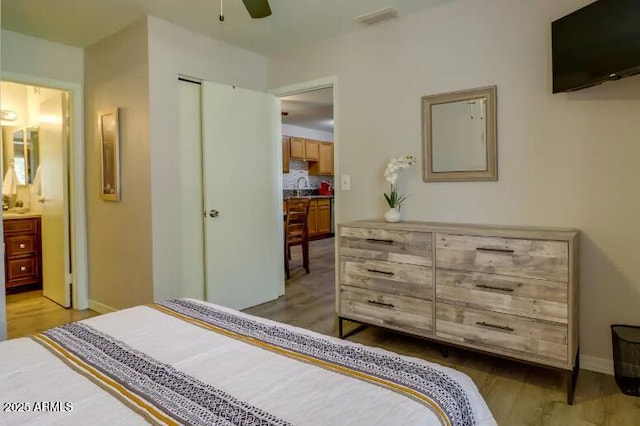 bedroom featuring a sink, ensuite bathroom, visible vents, baseboards, and light wood-style floors