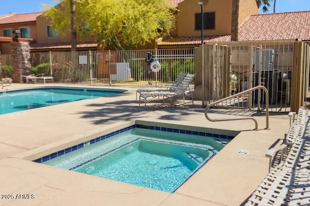 community pool with a hot tub, fence, and a patio area