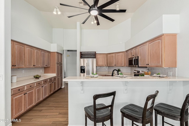 kitchen with a towering ceiling, a breakfast bar area, kitchen peninsula, stainless steel appliances, and light hardwood / wood-style flooring