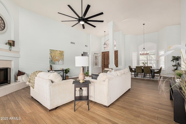 living room with a tiled fireplace, a towering ceiling, wood-type flooring, and ceiling fan with notable chandelier