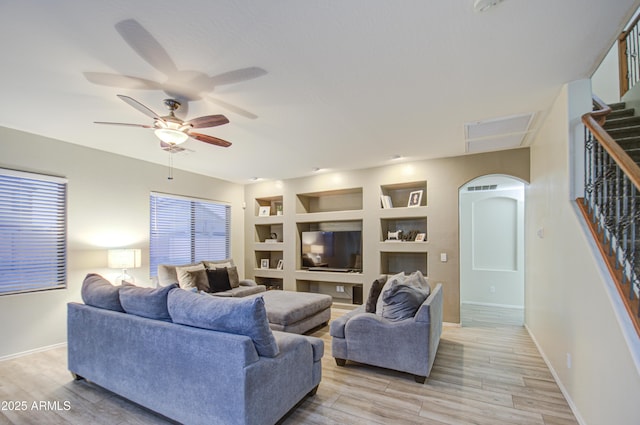 living room featuring built in shelves, light wood-type flooring, and ceiling fan