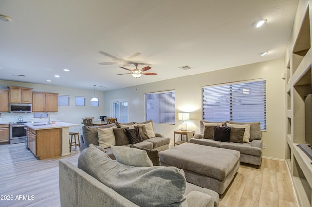 living room featuring ceiling fan, light hardwood / wood-style floors, and sink