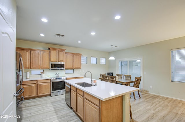 kitchen featuring stainless steel appliances, sink, light hardwood / wood-style flooring, a center island with sink, and pendant lighting