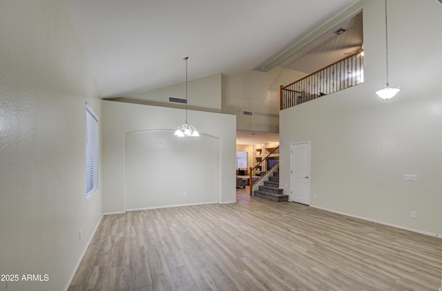 unfurnished living room featuring light wood-type flooring, an inviting chandelier, and high vaulted ceiling