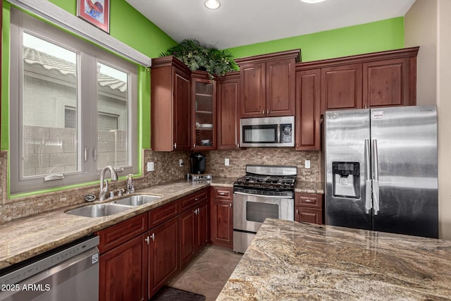 kitchen with tasteful backsplash, appliances with stainless steel finishes, light stone countertops, and sink