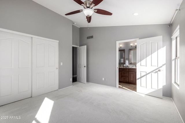 unfurnished bedroom featuring lofted ceiling, ensuite bath, ceiling fan, light colored carpet, and a closet