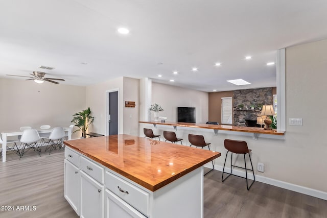 kitchen with a kitchen bar, butcher block counters, a skylight, hardwood / wood-style floors, and white cabinets