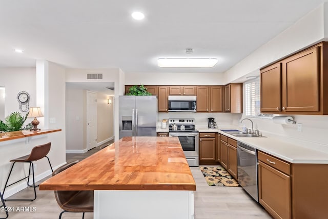 kitchen with butcher block countertops, sink, appliances with stainless steel finishes, a kitchen breakfast bar, and light hardwood / wood-style floors