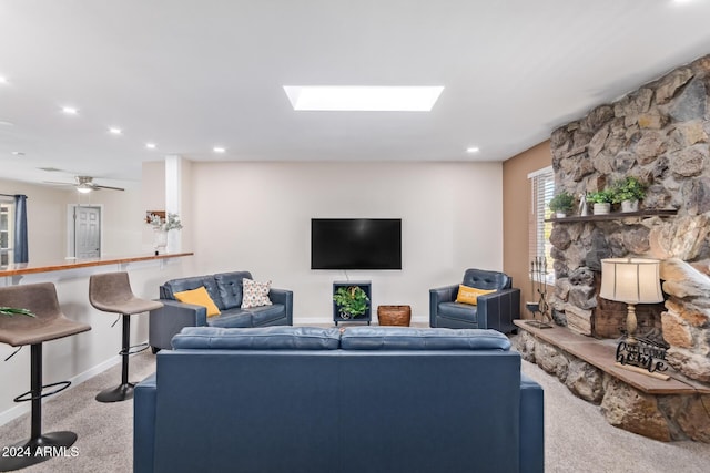 living room featuring a stone fireplace, a skylight, and carpet