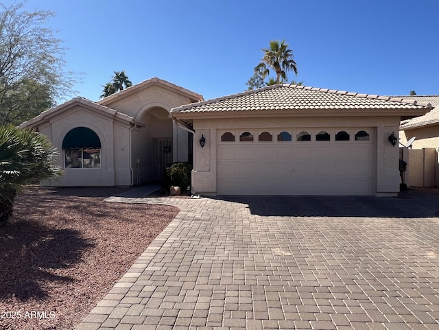 view of front of house featuring decorative driveway, an attached garage, a tile roof, and stucco siding