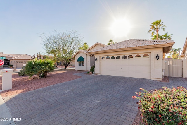 view of front of house with decorative driveway, a tile roof, stucco siding, an attached garage, and a gate