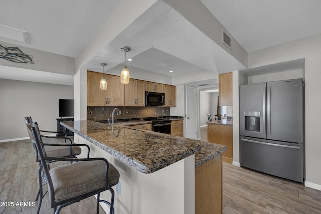 kitchen with pendant lighting, kitchen peninsula, black appliances, dark stone counters, and a breakfast bar