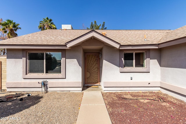 doorway to property featuring roof with shingles and stucco siding