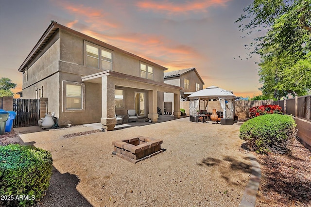 rear view of house featuring a patio, an outdoor fire pit, a fenced backyard, stucco siding, and a gazebo