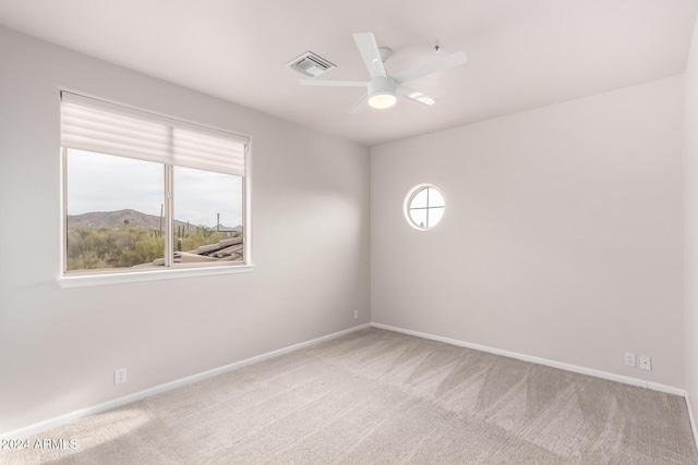 spare room with a mountain view, carpet floors, a healthy amount of sunlight, and ceiling fan