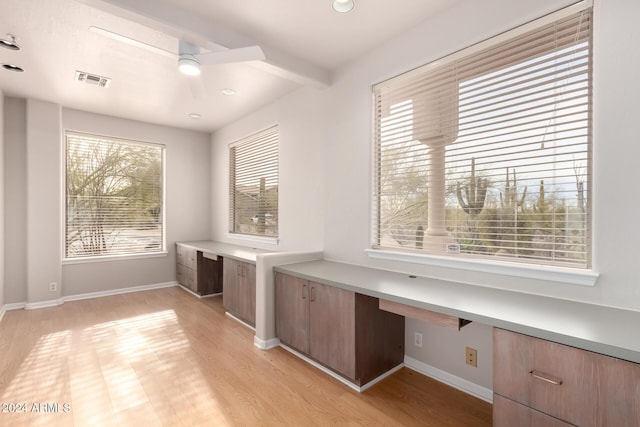 unfurnished office featuring light wood-type flooring, built in desk, ceiling fan, and beamed ceiling