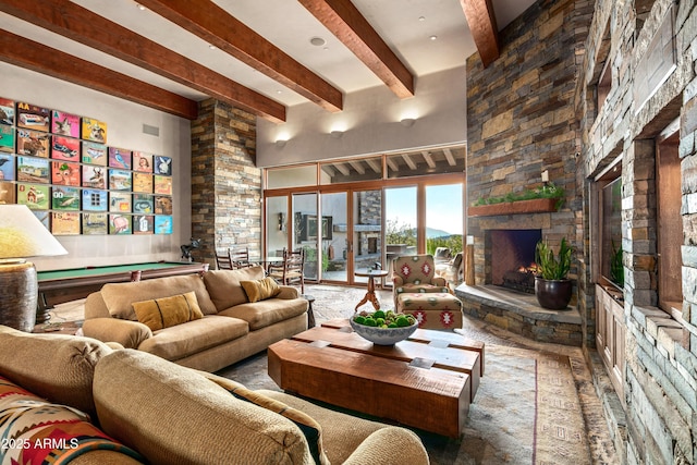 living room featuring beam ceiling, a stone fireplace, and pool table