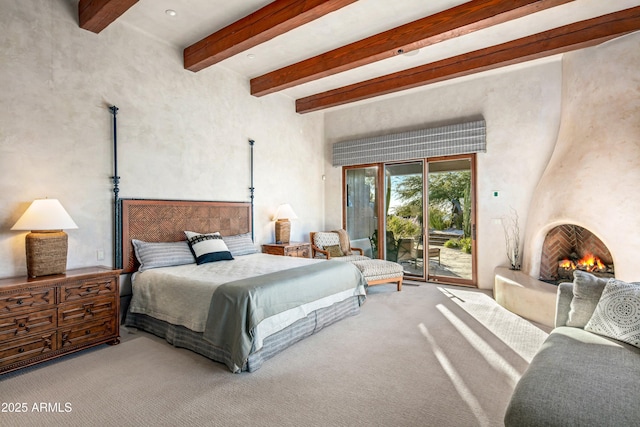 carpeted bedroom featuring beamed ceiling, a fireplace, and access to outside