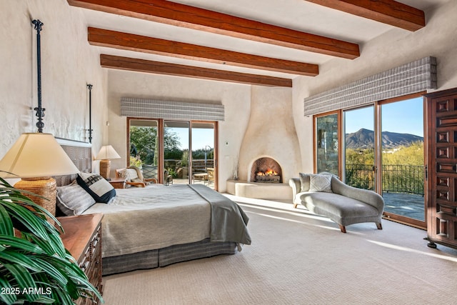 bedroom with access to exterior, carpet flooring, a large fireplace, beamed ceiling, and a mountain view