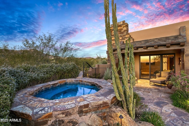 pool at dusk featuring a patio area and an in ground hot tub