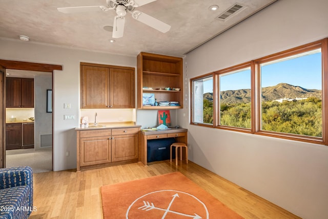 kitchen featuring ceiling fan, sink, light hardwood / wood-style flooring, a mountain view, and built in desk