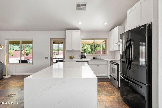 kitchen with sink, stainless steel range with electric cooktop, black fridge, light stone countertops, and white cabinets