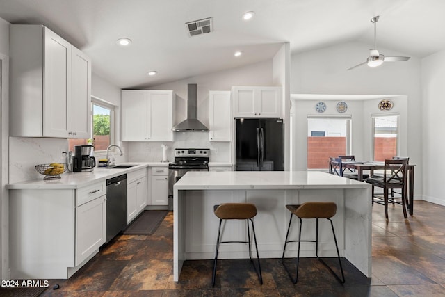 kitchen with vaulted ceiling, appliances with stainless steel finishes, white cabinetry, a center island, and wall chimney range hood